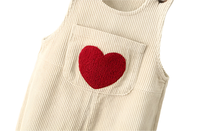 Close up of puffy heart on the front pocket of the cream baby corderoy pants.
