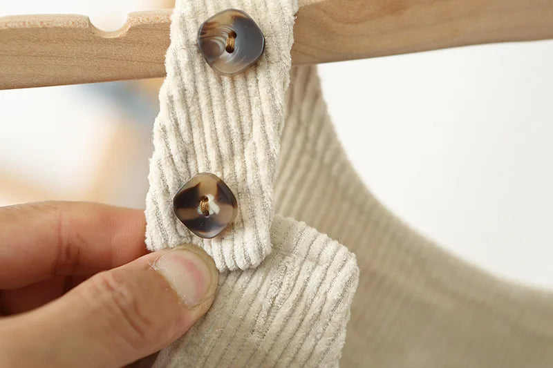 Close up of the toroise square buttons on the cream overalls made of corderoy.