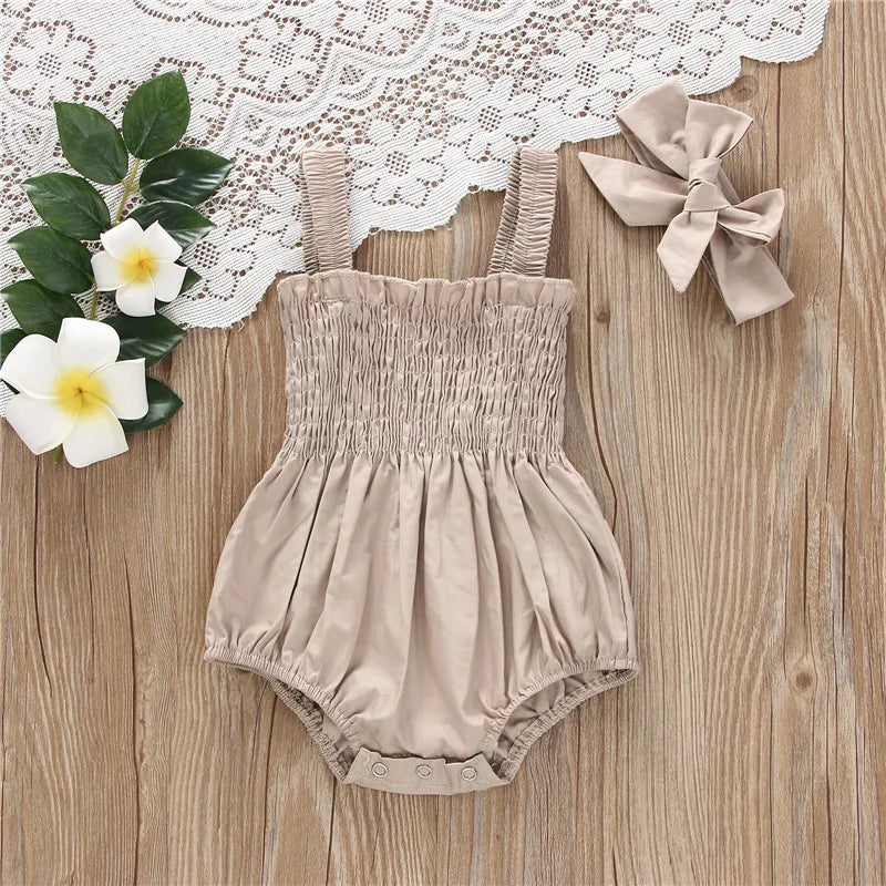 Beige infant romper with elastic straps at the shoulder a snap bottom and an elastic top with a bow.