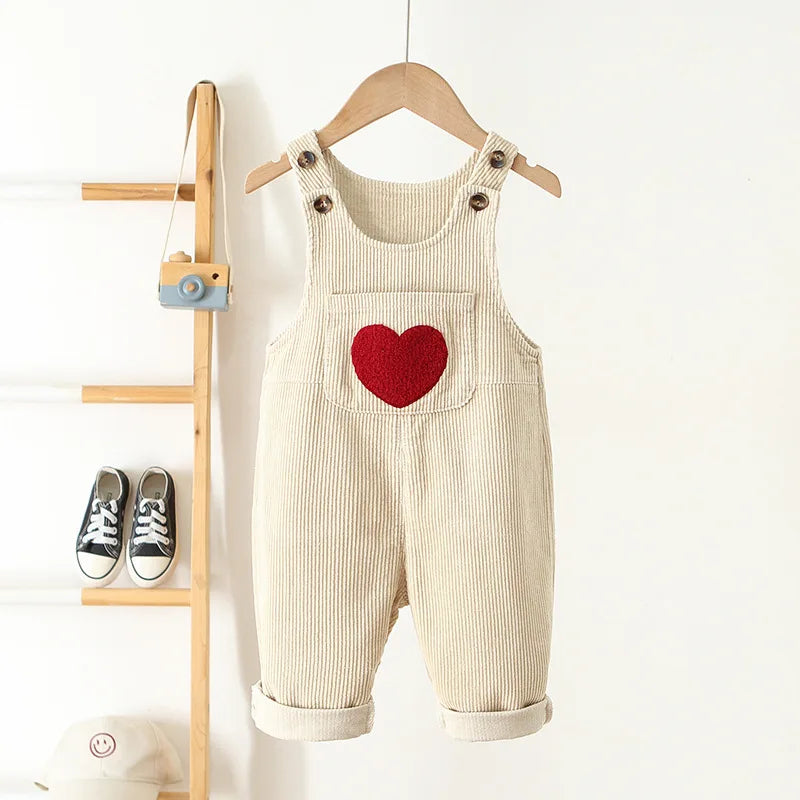 Cream baby and toddler overalls with a front pocket that has a red heart on the front. These baby overall pants have adjustable straps.