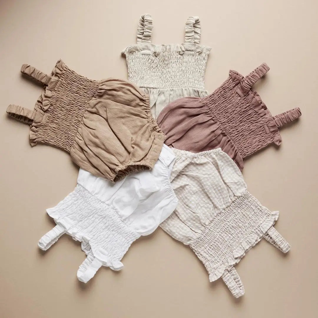Pink, Ivory, White and Beige  infant romper with elastic straps at the shoulder a snap bottom and an elastic top with a bow.