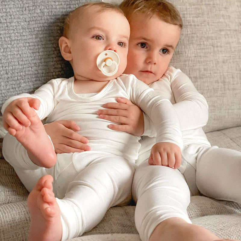 cozy kids pajamas. Baby and toddler sitting on a couch. The baby has a souther in his moth.