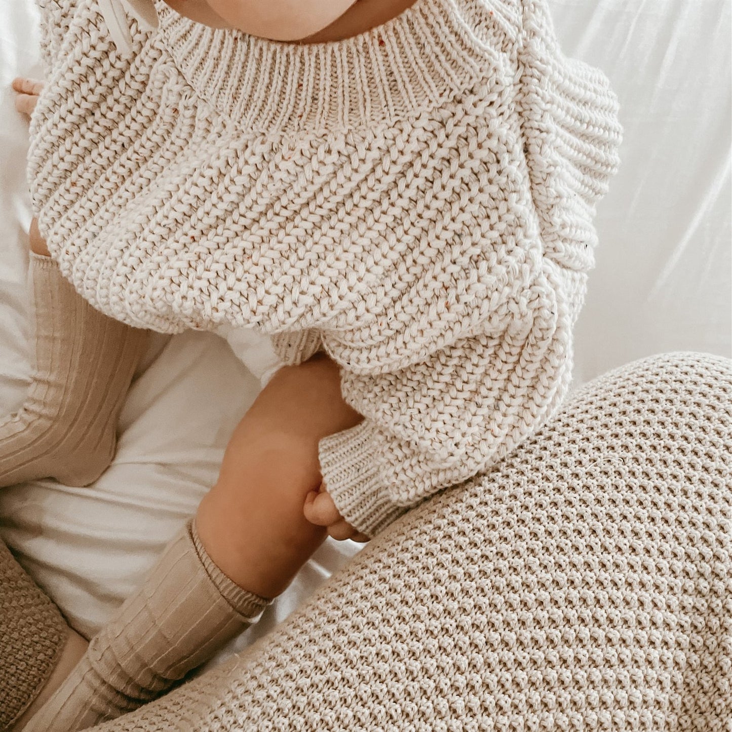 Top view of a baby wearing a light beige knitted sweater and beige knee socks.