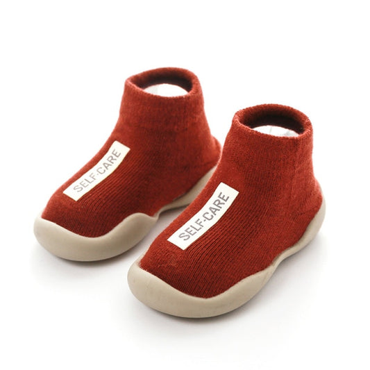Red first walker sock shoes with a self care lable on the top of the arch.