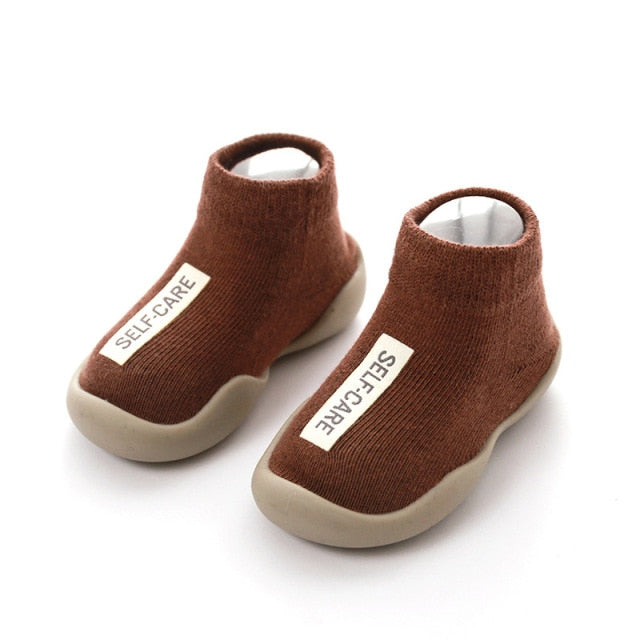 Brown first walker sock shoes with a self care lable on the top of the arch.