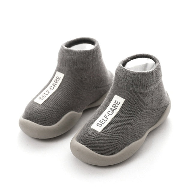 Grey first walker sock shoes with a self care lable on the top of the arch.
