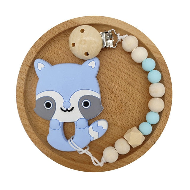 Blue Raccoon Silicone and Wood Pacifier Clip and teether set in wooden circular tray