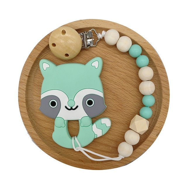 Green Raccoon Silicone and Wood Pacifier Clip and teether set in wooden circular tray