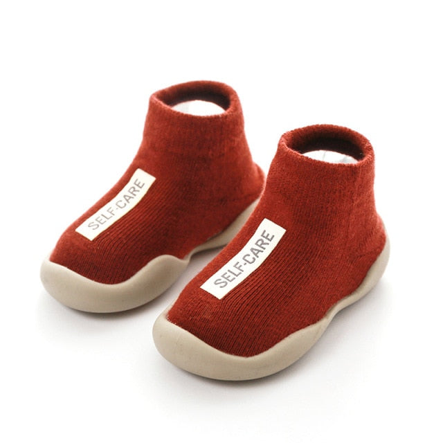 Red first walker sock shoes with a self care lable on the top of the arch. 