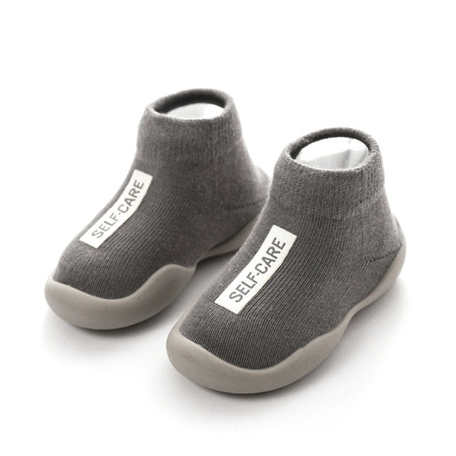 Grey first walker sock shoes with a self care lable on the top of the arch. 