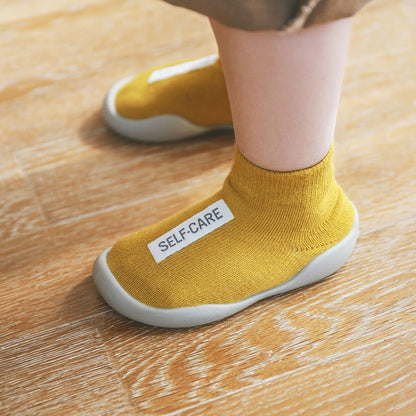 Yellow first walker sock shoes with a self care lable on the top of the arch. 