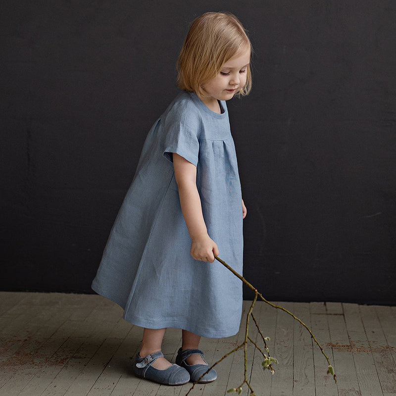 little girl holdng a stick posing for a picture wearing a baby blue linen dress