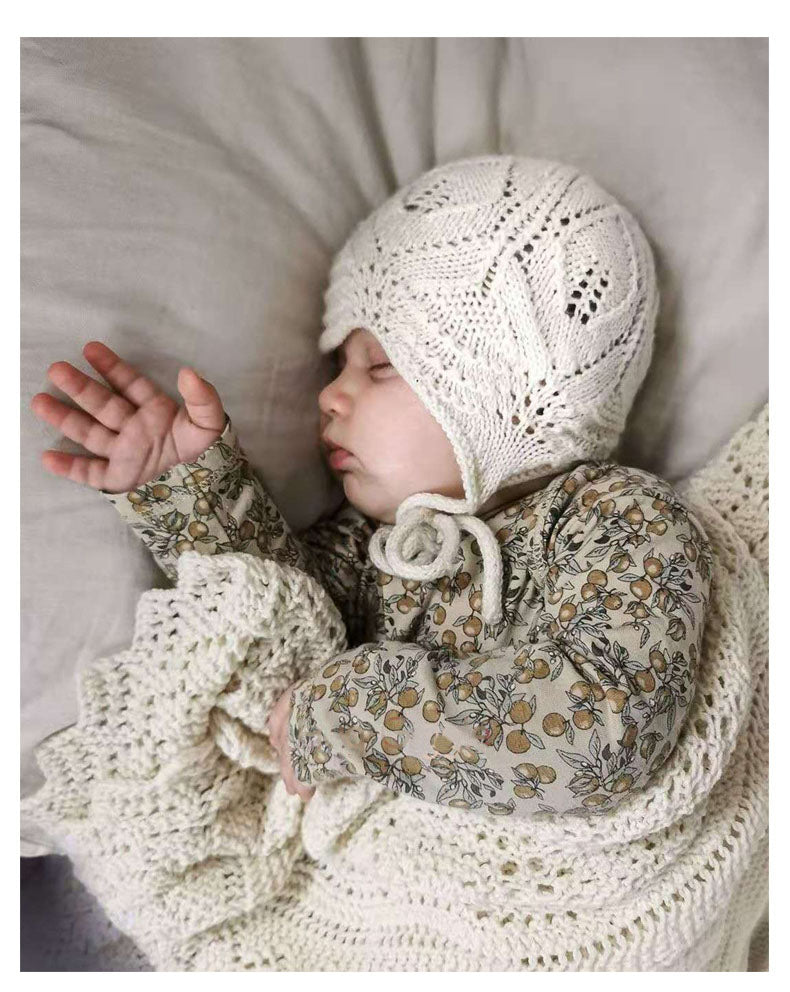 Newborn wearing a matching knitted hat and blanket wearing 2 Piece set, long sleeved onesie with side and bottom snaps and leggings with berry pattern.