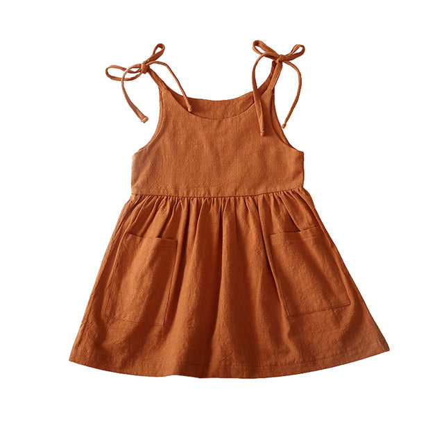 summer toddler dress with ties at the shoulder, ruffled skirt, and front pockets in rust. 